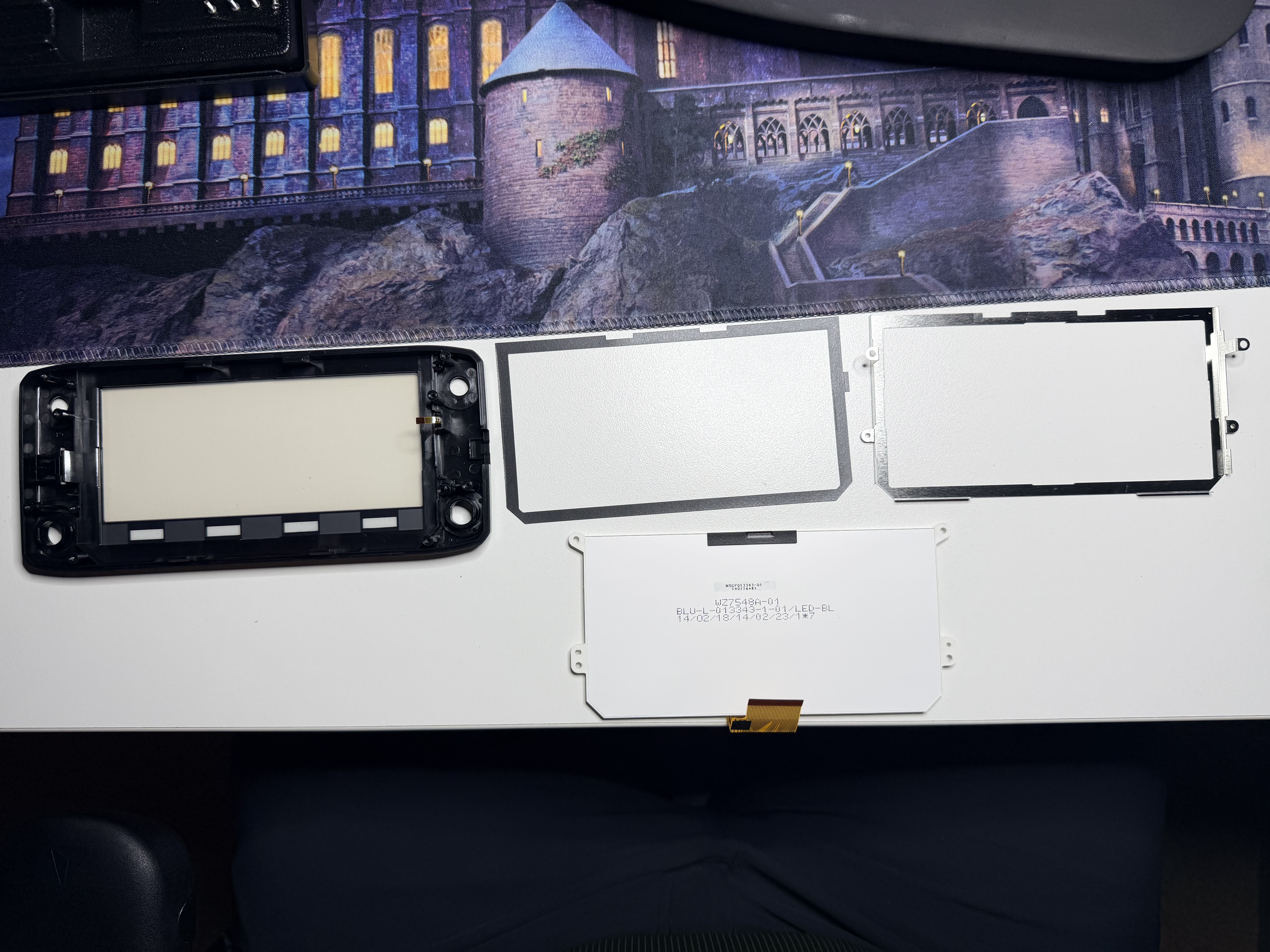 Old display assembly removed with replacement parts laid out beside the front bezel.